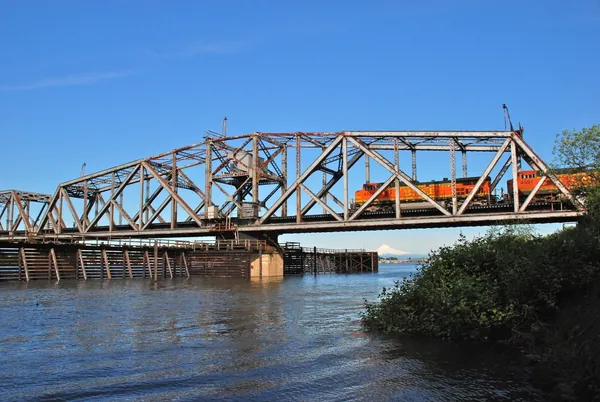A BNSF freight train crossing a steel railroad bridge above blue water.