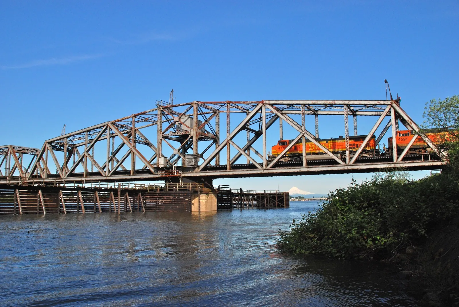 A BNSF freight train crossing a steel railroad bridge above blue water.