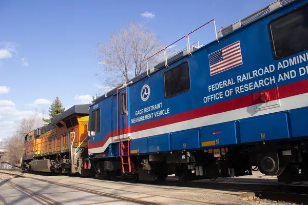The blue, red, and white FRA DOTX-218 gauge restraint measurement vehicle.