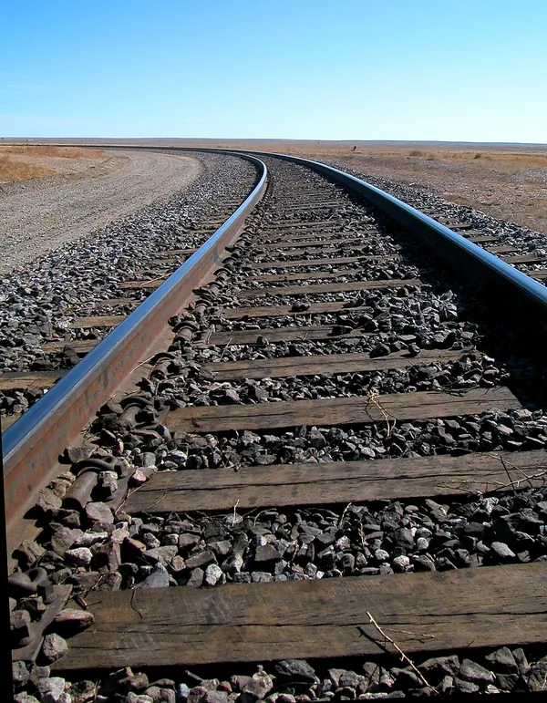Timber railroad ties and ballast beneath two rails curving across open terrain.